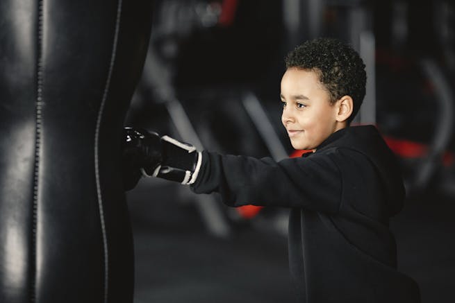 A young boy smiling while training with a punching bag in a gym setting.